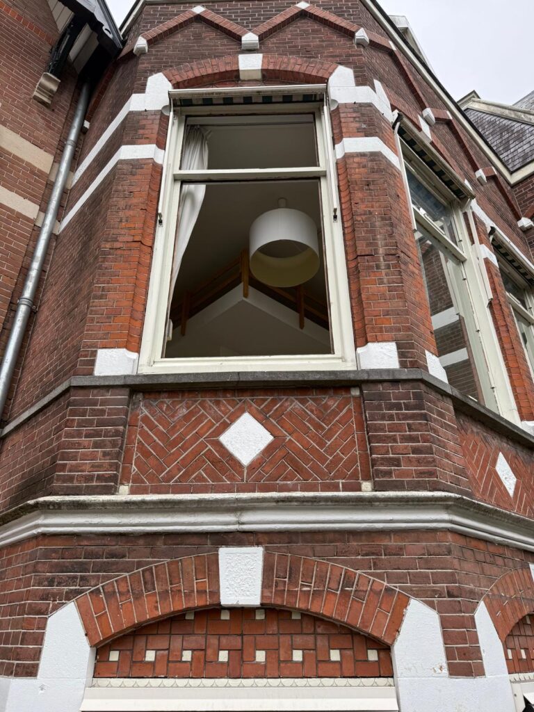 Houten raam met bovenlicht in een karakteristieke bakstenen erker