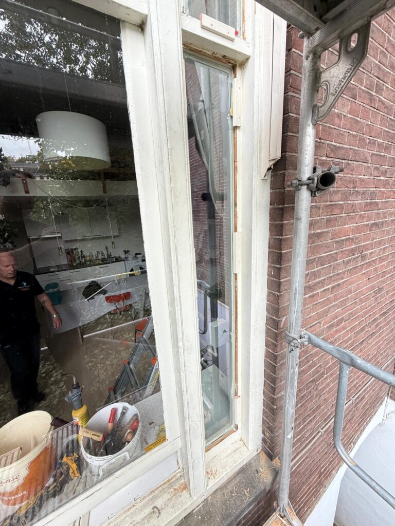 Werkzaamheden aan een houten raam met gereedschap en een steiger
