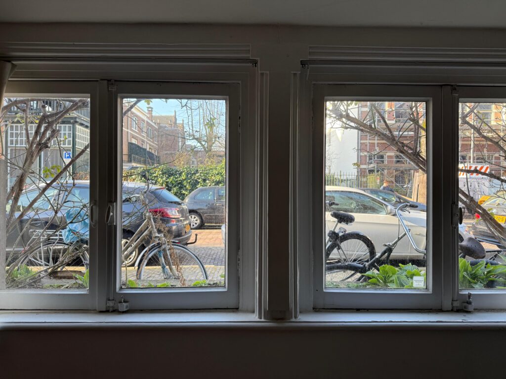 Woonkamerramen met uitzicht op geparkeerde auto’s en fietsen aan de straat