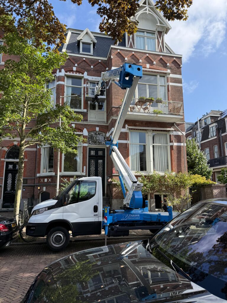 Montagewagen met hijsarm opgesteld aan de straat voor een woning