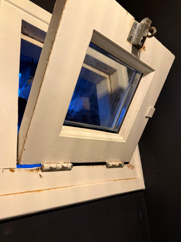 Detail van een geopend wit houten raam met beglazing en scharnieren